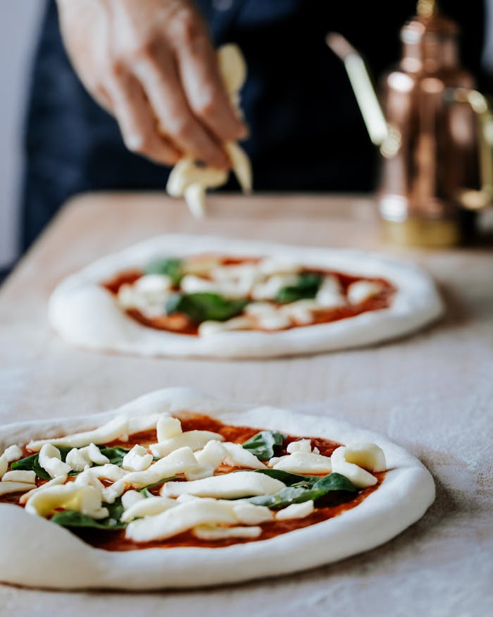 A close-up of a hand preparing Neapolitan pizza with fresh toppings in a London kitchen.